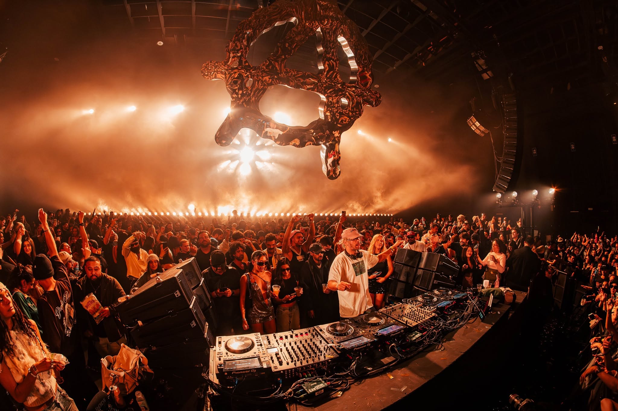A packed dance floor under amber light, with PK line arrays flown over the room